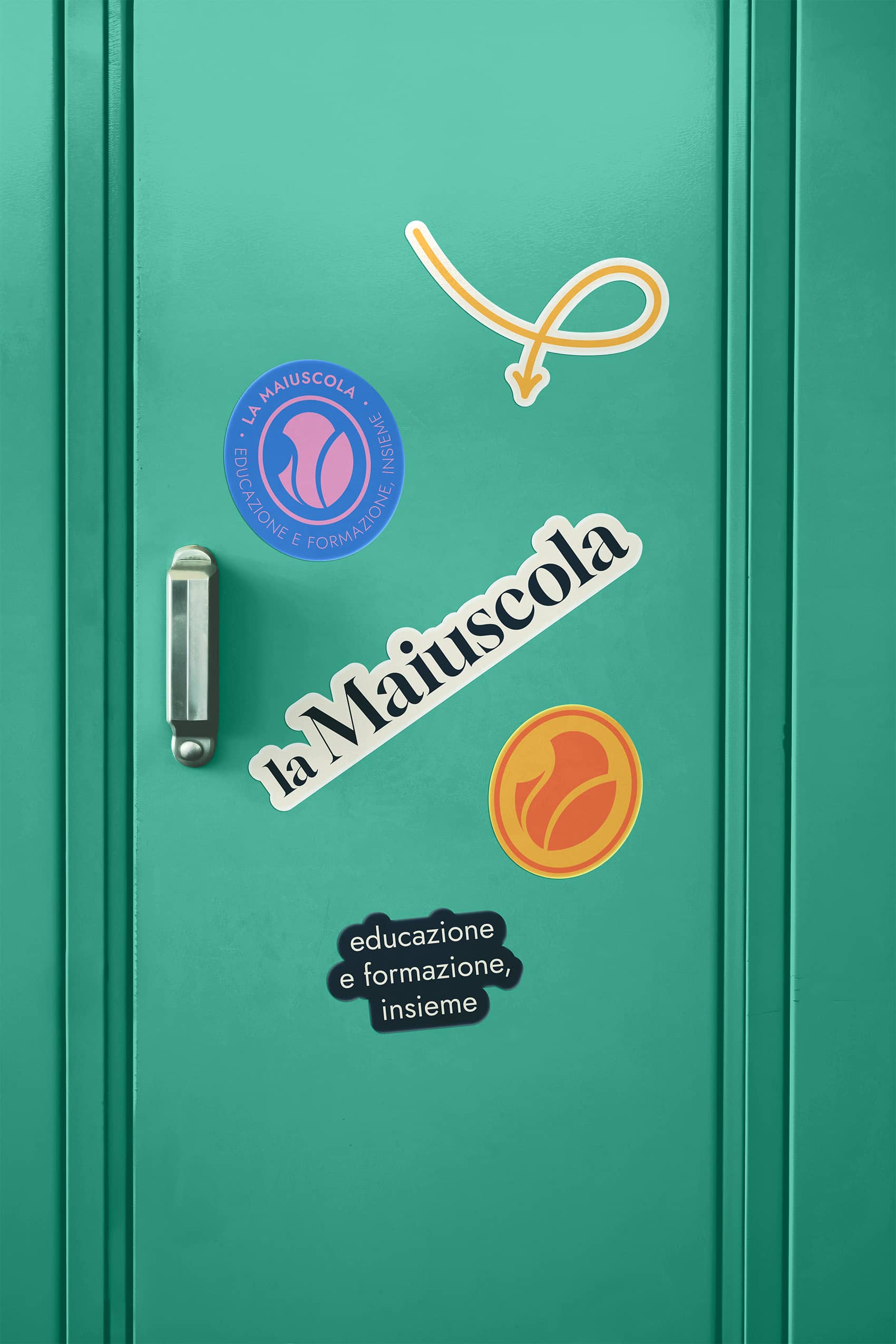 Green locker door with stickers including a blue circular logo, yellow-orange circular logo, black sticker reading 'educazione e formazione, insieme', a white sticker with 'la Maiuscola', and an orange arrow.