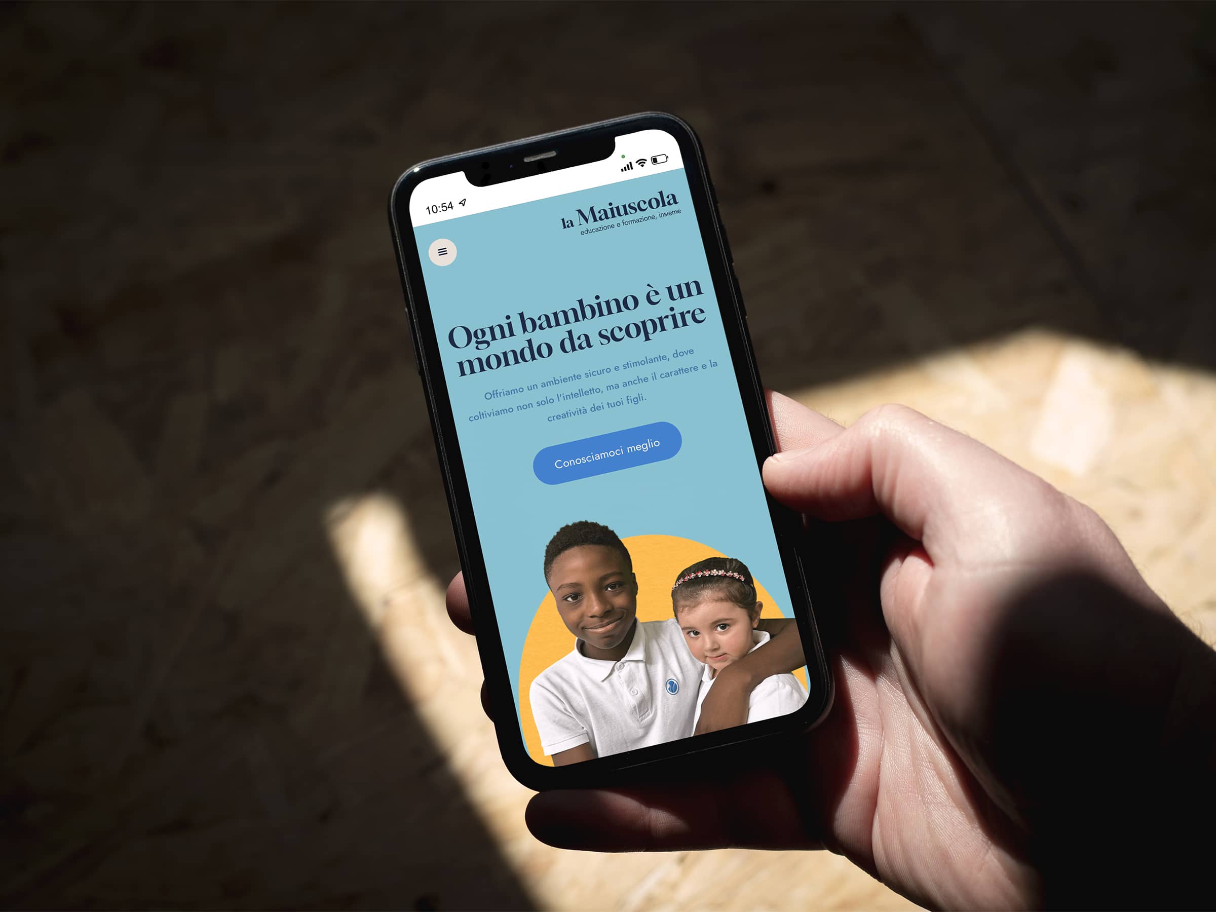 Hand holding a smartphone displaying an educational website with text in Italian and images of two children.