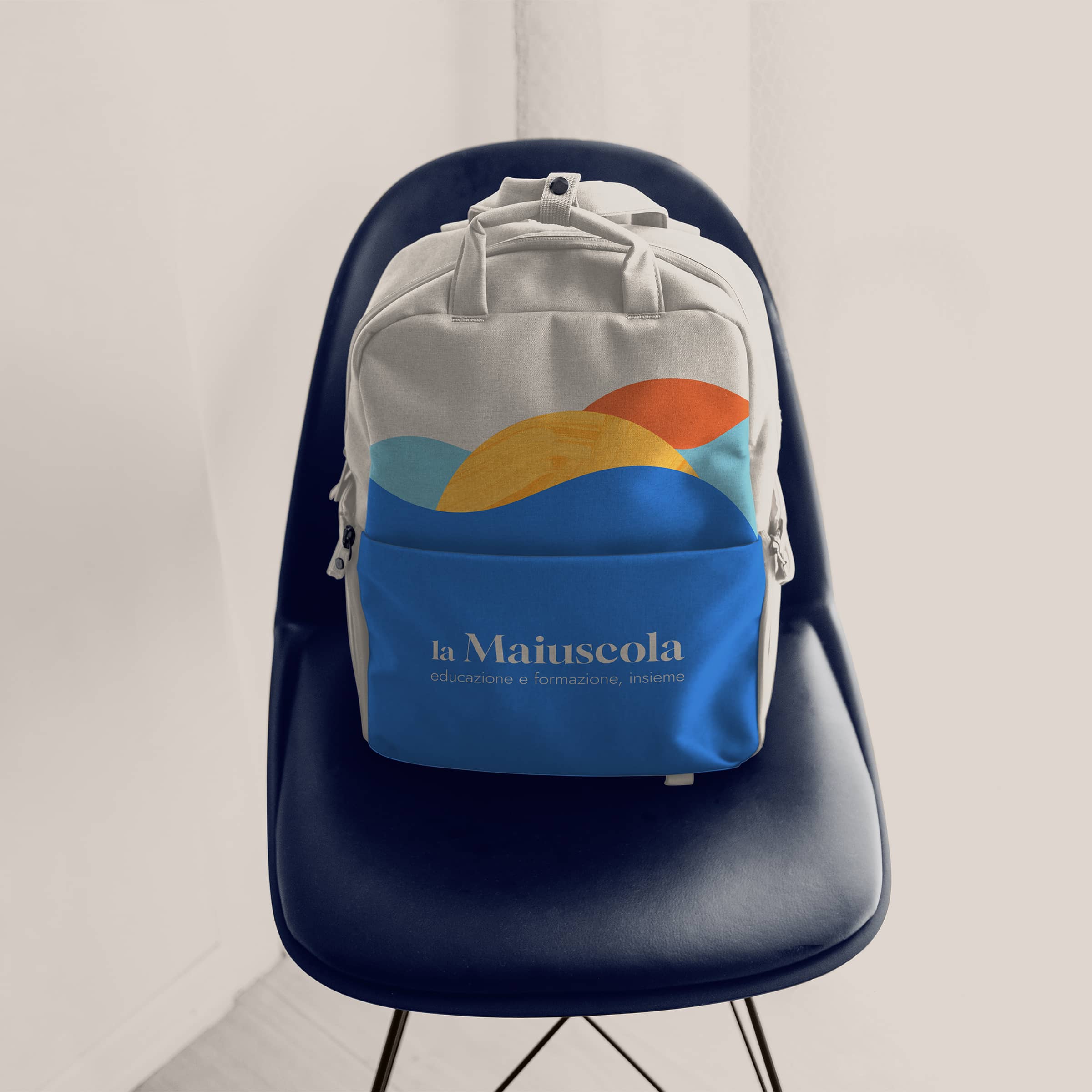Beige backpack with colorful abstract waves and Italian text on the front pocket, placed on a dark blue chair.