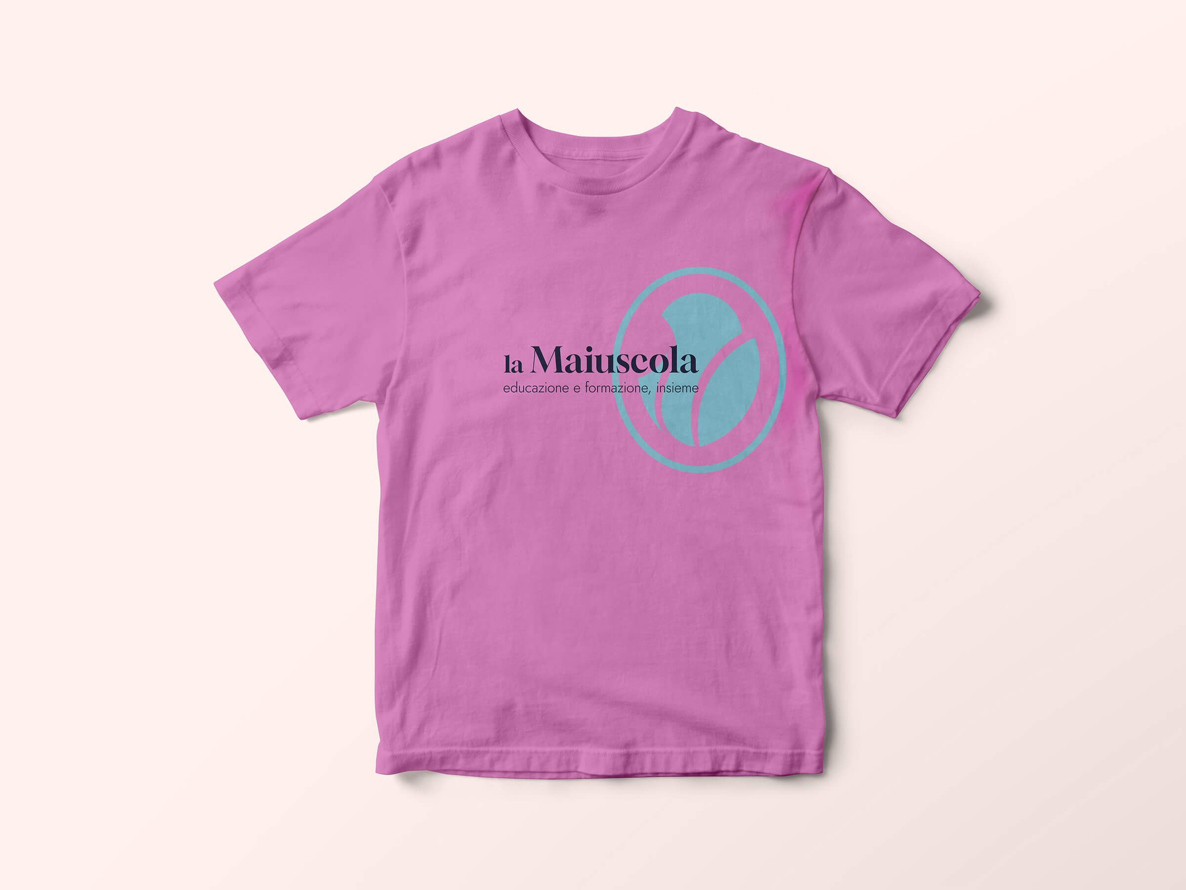 Pink t-shirt with a turquoise circular logo and the text 'la Maiuscola educazione e formazione, insieme' printed on the front.